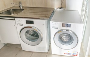Two white Miele washing machines in a kitchen with a stainless steel sink and a tiled backsplash. - Lovely home in Bankeryd with lake view (Bankeryd)