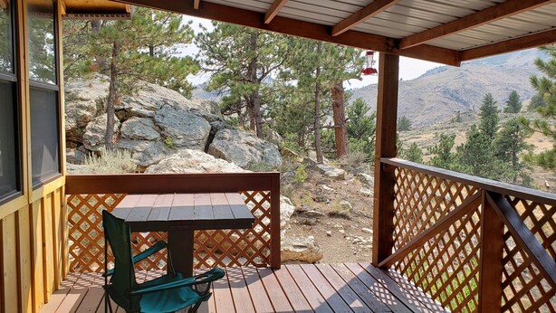 A wooden deck with a table and chairs, overlooking a rocky landscape with trees and mountains. - Remote peaceful cabin,  great wildlife viewing, hunting and fishing close by (Wheatland)