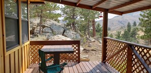 A wooden deck with a table and chairs, overlooking a rocky landscape with trees and mountains. - Remote peaceful cabin,  great wildlife viewing, hunting and fishing close by (Wheatland)