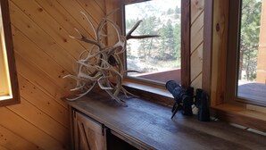 A wooden interior with a large window, a deer antler sculpture, and a telescope on a wooden table. - Remote peaceful cabin,  great wildlife viewing, hunting and fishing close by (Wheatland)