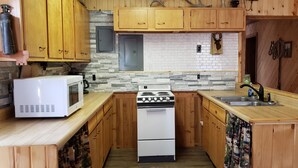 A compact kitchen with wooden cabinets, a white stove, a microwave, and a sink. - Remote peaceful cabin,  great wildlife viewing, hunting and fishing close by (Wheatland)