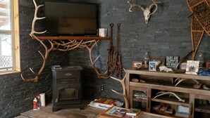 A room with a fireplace, a television mounted on a wooden stand, and antler decorations on the walls. - Remote peaceful cabin,  great wildlife viewing, hunting and fishing close by (Wheatland)