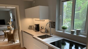 Eine moderne Küche mit einem schwarzen Induktionskochfeld, weißen Schränken, einer integrierten Spüle und einem Fenster mit Blick ins Grüne.