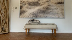 Ein Zimmer mit großem Meeresblick-Gemälde, einer Bank mit gemustertem Tischläufer und einem hölzernen Dekorationsgegenstand.