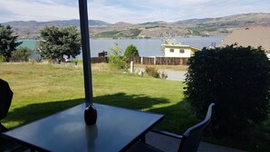 Un patio con mesa y sillas que da a un lago y colinas.