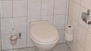 Ein kleines Badezimmer mit Toilette, einem Handtrockner, einem Toilettenpapierhalter und einem kleinen Topf mit Pflanze.