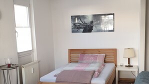 Ein Schlafzimmer mit einem Bett, einem Nachttisch, einer Lampe, einer Heizung, einem Fenster und einem Sofa.