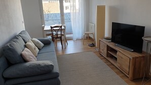 Ein Wohnzimmer mit grauem Sofa, Holz-TV-Möbel und einem Esstisch mit Stühlen.