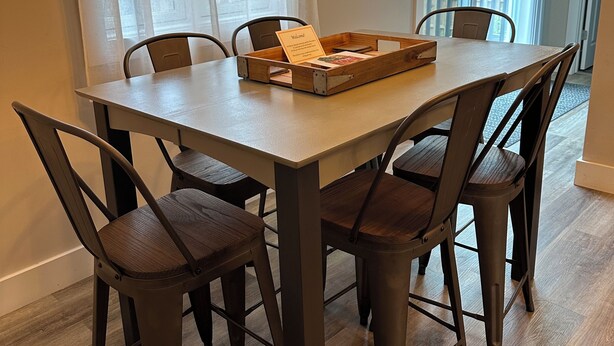 A dining area with a wooden table and chairs, a welcome sign, and a framed quote on the wall. - In the Heart of Three Oaks - Steps to Downtown (Three Oaks)