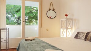 Un dormitorio con cama, ventana con vista a árboles, puerta y un pequeño armario blanco.