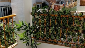Een balkon met een bloempot, een metalen hek en vloertegels met een patroon.