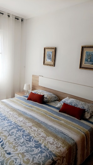 A hotel room with a bed, two pillows, a bedside table with a lamp, and two framed pictures on the wall. - A beautiful bungalow (Torrevieja)