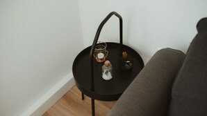 Une petite table d’appoint noire, sur laquelle on a posé une bougie, un bocal en verre et un objet décoratif, le tout adossé à un mur blanc.