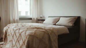 Une chambre à coucher avec un lit, une fenêtre avec des rideaux et une lampe de chevet.