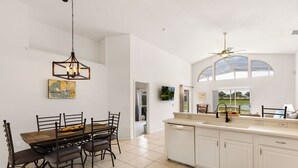 A modern kitchen with white cabinetry, a dining area with a wooden table and chairs, and a large window providing natural light.