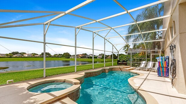 A covered swimming pool with a hot tub, surrounded by a white fence, and a view of a residential area.
