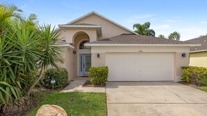 A single-story house with a garage, a front door, and a small front yard with a palm tree and a rock.
