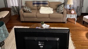 A living room with a beige sofa, a TV mounted on the wall, a ceiling fan, and a wooden coffee table. - Cozy 3 Bedroom Port Clinton House (Port Clinton)