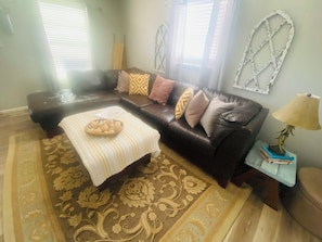 A living room with a brown leather sofa, patterned rug, and a small table with a lamp.