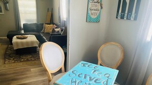 Un comedor con una mesa y sillas, un cartel decorativo en la pared, y un sofá al fondo.