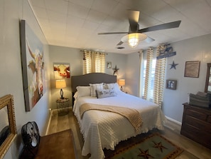 A bedroom with a large bed, a ceiling fan, and a view of the outdoors through the window.