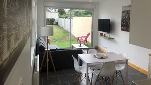 Uma sala de estar moderna com um sofá, uma mesa de jantar e uma televisão fixada na parede.