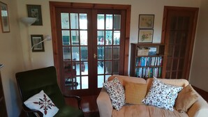 A living room with a green armchair, a beige sofa with floral cushions, a wooden door with glass panels, and a bookshelf with books. - Perfectly located for The Pentlands. It also has easy access to the city. (Edinburgh)