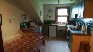 A compact kitchen with a microwave, sink, and small refrigerator. There is a colorful table with a quilted tablecloth and a wooden stool. - Perfectly located for The Pentlands. It also has easy access to the city. (Edinburgh)