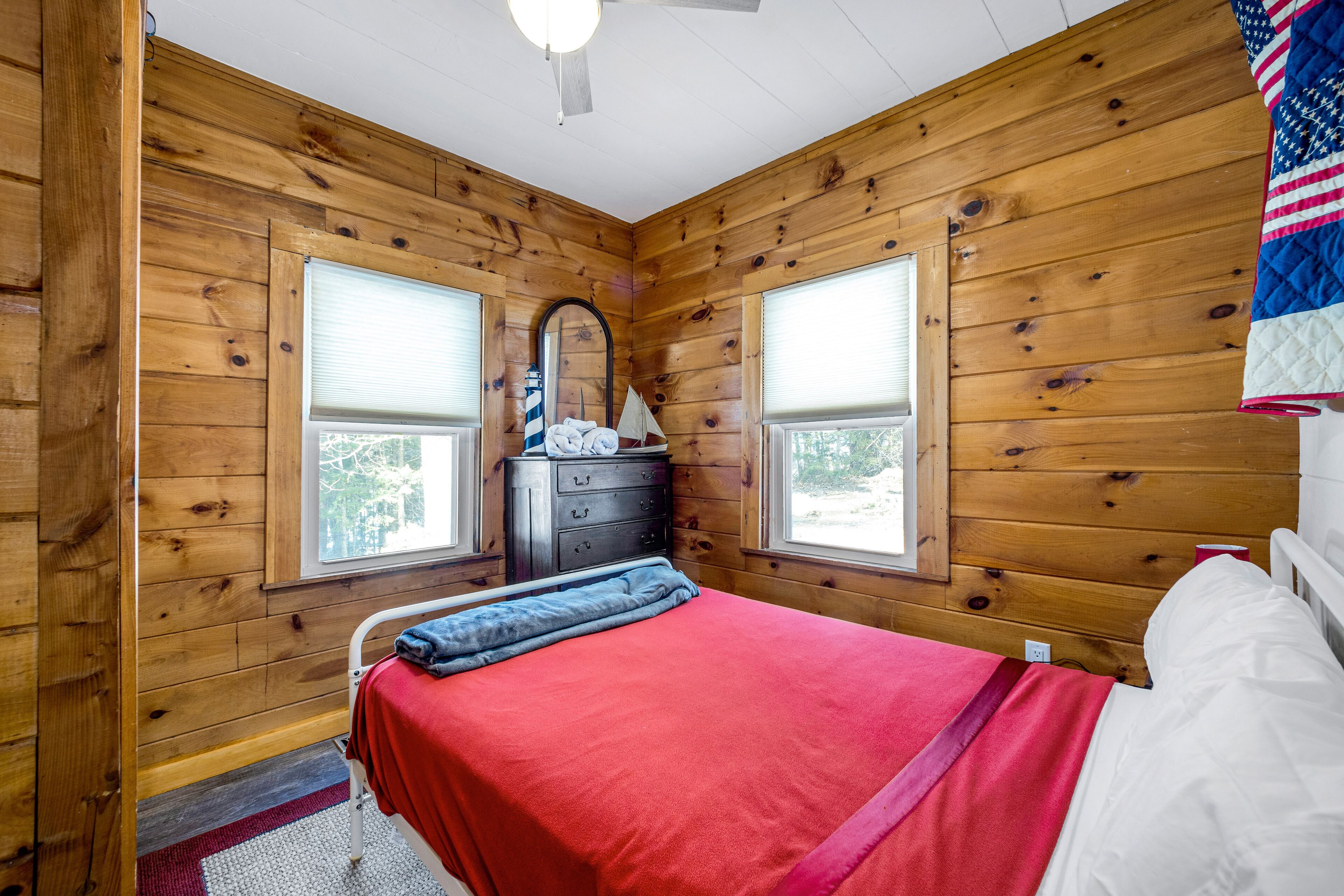 Una camera da letto in una baita di legno, con un letto, una cassettiera e finestre.