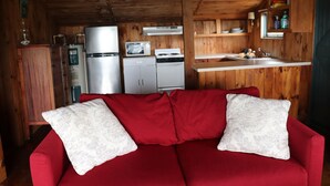 A compact cabin-style room with a red sofa, wooden walls, a kitchenette with a stove, microwave, and refrigerator, and a small window. - Cozy Cottage   with spectacular salt water  view / 4 Kayaks available/ (Bremen)