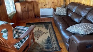A cozy cabin interior with a wooden ceiling, a leather sofa with patterned cushions, a wooden chair with a checkered cushion, and a framed picture on the wall. - Cozy Cottage   with spectacular salt water  view / 4 Kayaks available/ (Bremen)