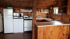 A wooden cabin kitchen with a refrigerator, stove, microwave, sink, and wooden cabinets. - Cozy Cottage   with spectacular salt water  view / 4 Kayaks available/ (Bremen)