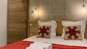 Et hotelværelse med en trædør, en seng med rødt sengetøj og to dekorative puder, samt to vægmonterede lamper.