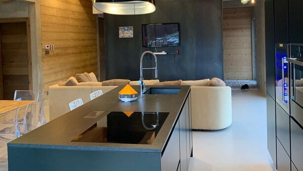 Et moderne køkken med en central ø, indbygget ovn og en stor sort hængende lampe.