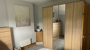 A bedroom with a bed, a wooden wardrobe, a dresser, a radiator, and a small sink.