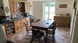 A kitchen with wooden cabinets, a dining table, chairs, a washing machine, and a large window.