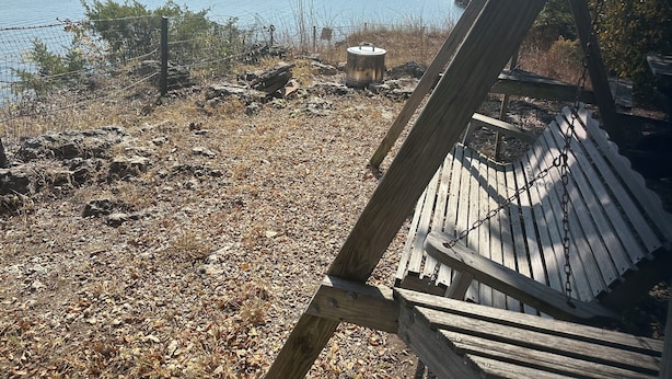 Een houten schommelstoel met uitzicht op een meer met een rotsachtige oever en een metalen bak.