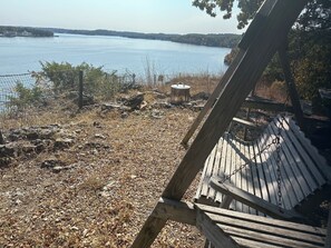 A wooden swing chair overlooking a lake with a rocky shore and a metal container. - Located on a bluffcliff, 80 ft off the water with a magnificent view of the Lake (Sunrise Beach)