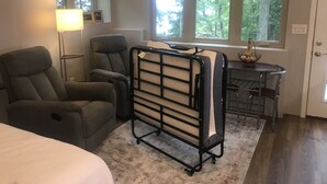 Een kamer met een bed, twee fauteuils, een bureau met stoel, een radiator en grote ramen met zonwering.