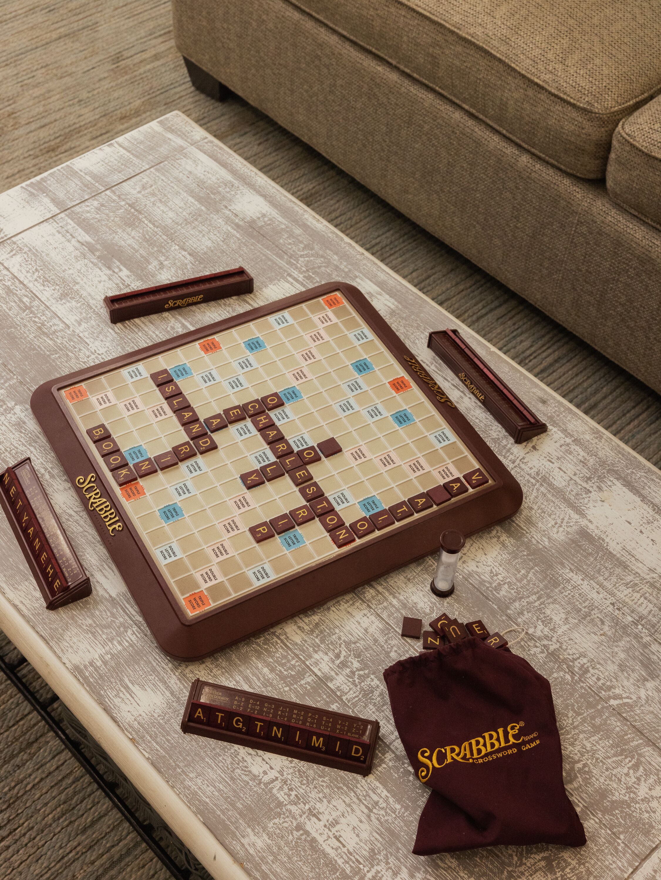 Un joc de Scrabble damunt un taula de fusta amb un sofà al fons.