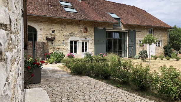A stone house with a tiled roof, a paved driveway, and a garden with various plants and flowers. - Large, bright designer country house (La Chailleuse)