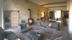 A cozy living room with a stone wall, a fireplace, leather sofas, and a dining area. - Large, bright designer country house (La Chailleuse)