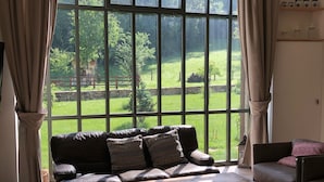 A living room with a large window, a sofa, a coffee table, and a view of a green landscape. - Large, bright designer country house (La Chailleuse)