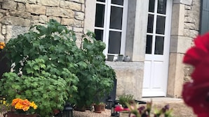 A stone building with a large window and a door, surrounded by potted plants and a gravel pathway. - Large, bright designer country house (La Chailleuse)