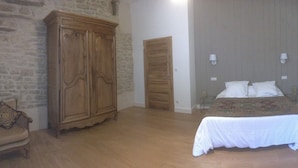 A bedroom with a wooden wardrobe, a bed with white bedding, and a stone wall. - Large, bright designer country house (La Chailleuse)