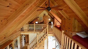 Une chambre mansardée en bois, dotée d’un ventilateur de plafond, d’un espace de couchage en mezzanine et d’un escalier.
