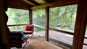 Une terrasse en bois avec une chaise rouge et un banc, donnant sur une zone boisée.