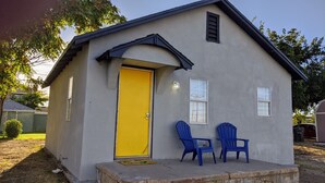 Une petite maison de plain-pied avec une porte jaune et deux chaises bleues devant.