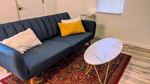 Un canapé bleu foncé agrémenté de deux coussins, une petite table ronde blanche aux pieds dorés et un tapis à motifs.