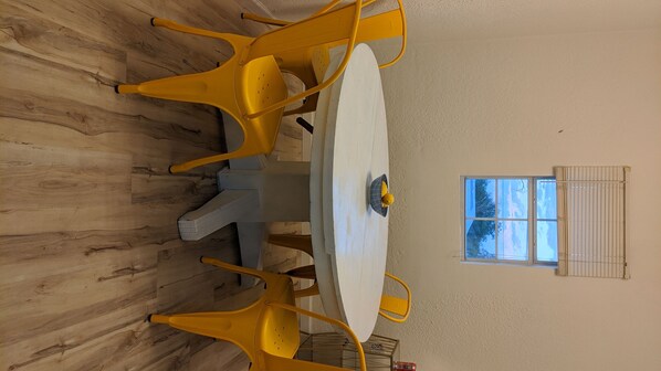 A dining table with yellow chairs, a white tablecloth, and a window with blinds.